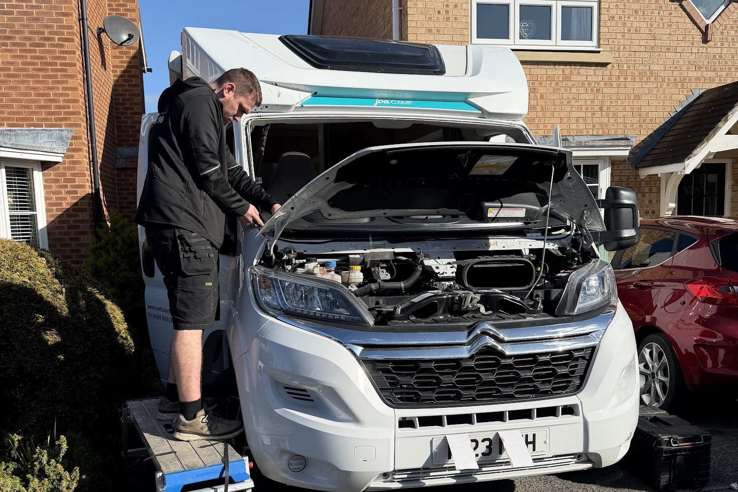 Fitter working on a motorhome with its windscreen out, on a customer's driveway